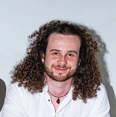 Maciej Czerniak, lachend, met lang krullend haar en een wit shirt.